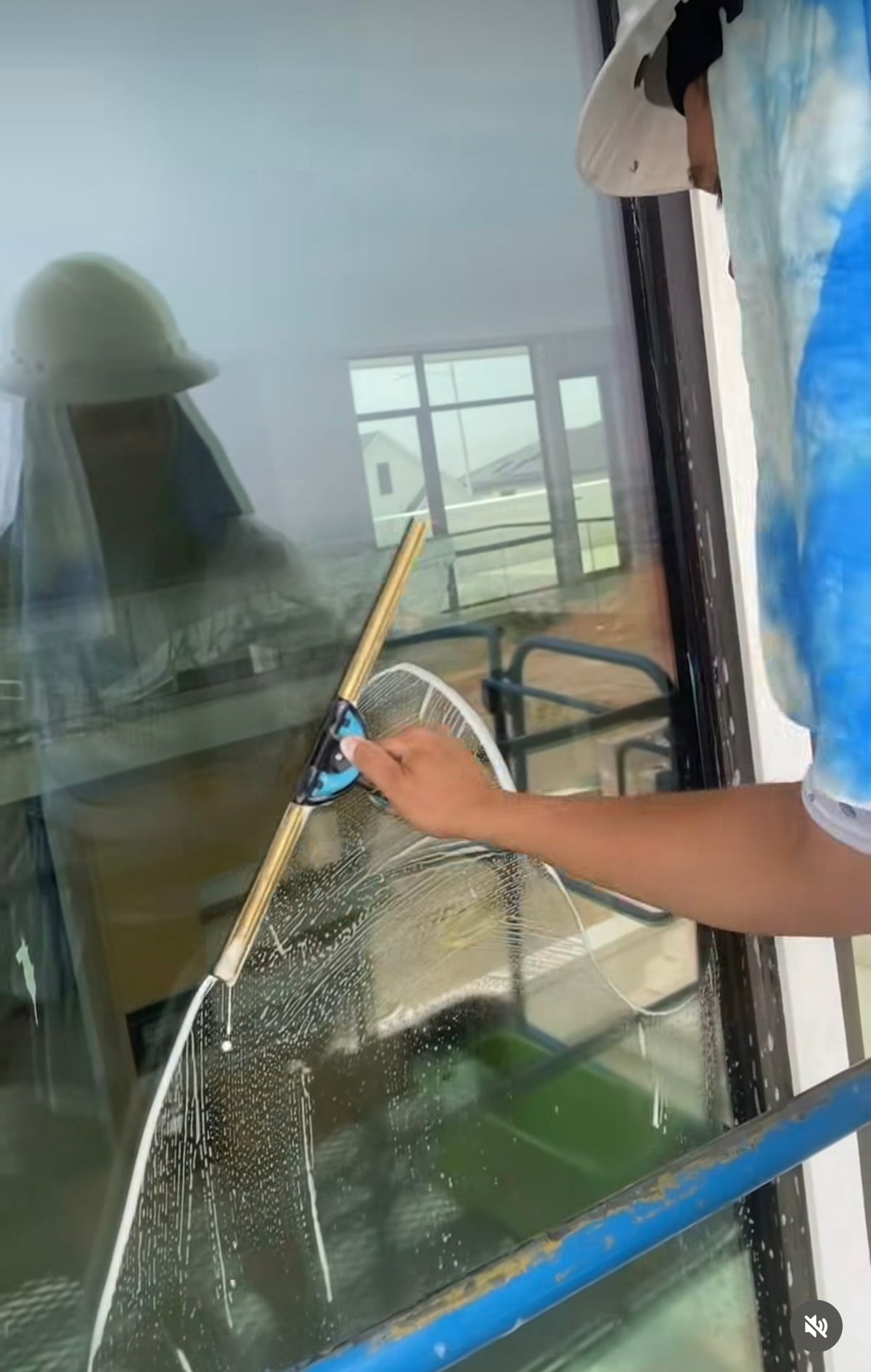 Reflection in freshly-squeegeed glass shows the operator in a boom-lift basket 20 feet up and 50 feet out over a swimming pool